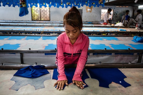Phnom Penh, Cambodia, 3 april 2015, this garment worker prepares shirts and puts them on a long row for making prints on them, while the smell of dying penetrates the nose,  at a subcontractor with no name on the front door.  A high number of not registered garment  factories, operating in a legal vacuum, fulfill orders from registered factories. This picture was shot because the manager let us in, but we had to flee when the boss was comming, as illegal factory owners don't want any journalists around.